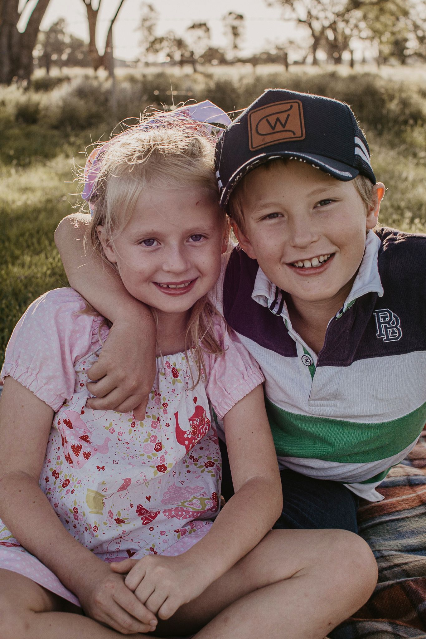 Brother & Sister sitting down in a rural landscape, smiling and relaxed.