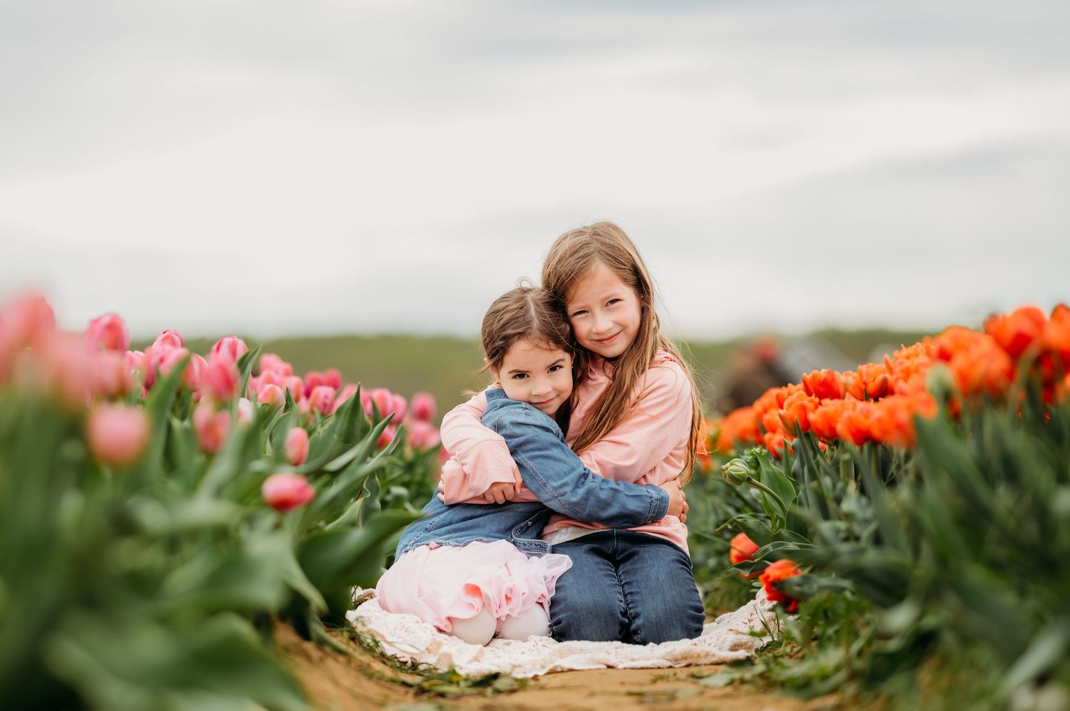 Two sisters sit together surrounded by colorful blooming tulips in a field at Holland Ridge Farms