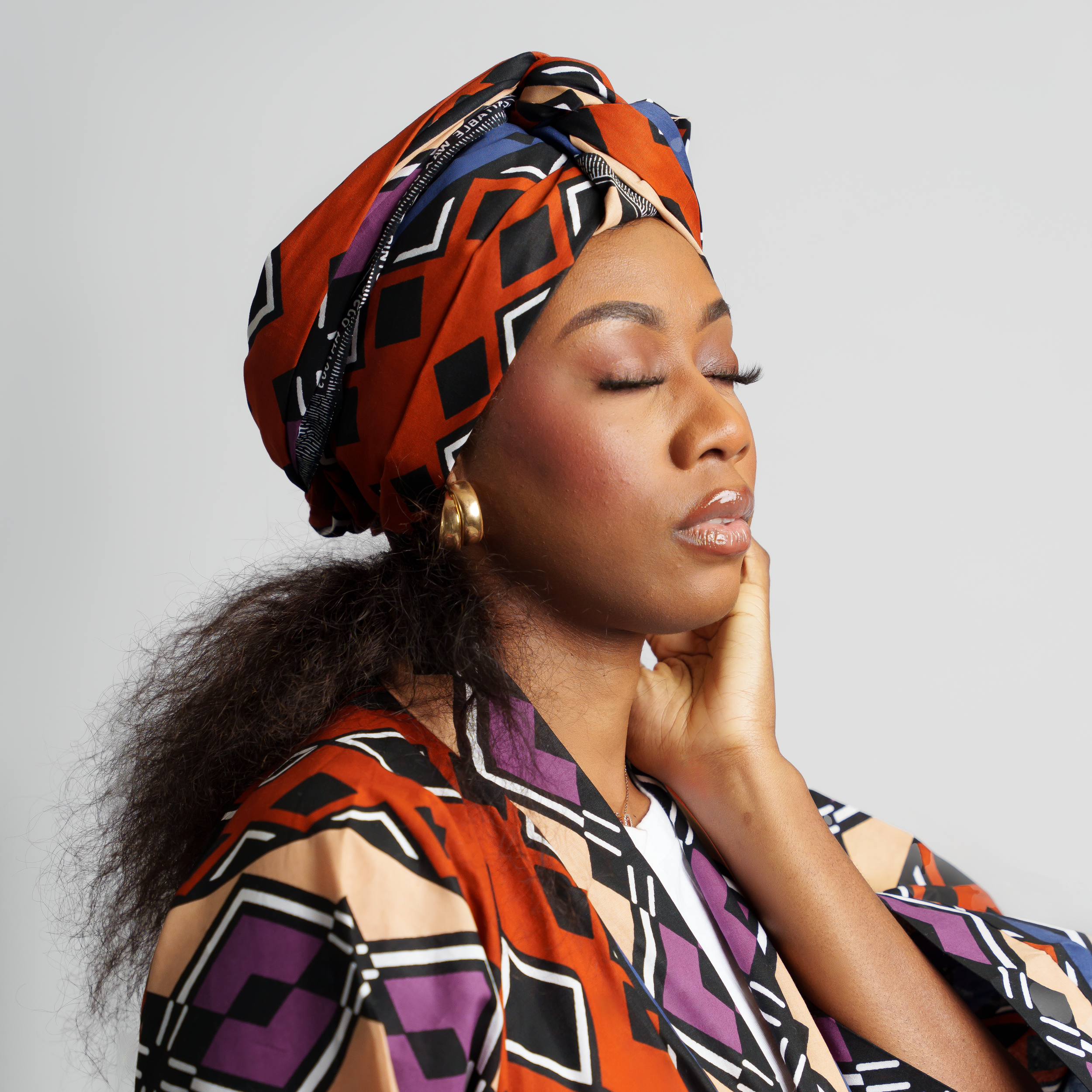 Artistic portrait featuring orange and purple geometric print headwrap and matching outfit.