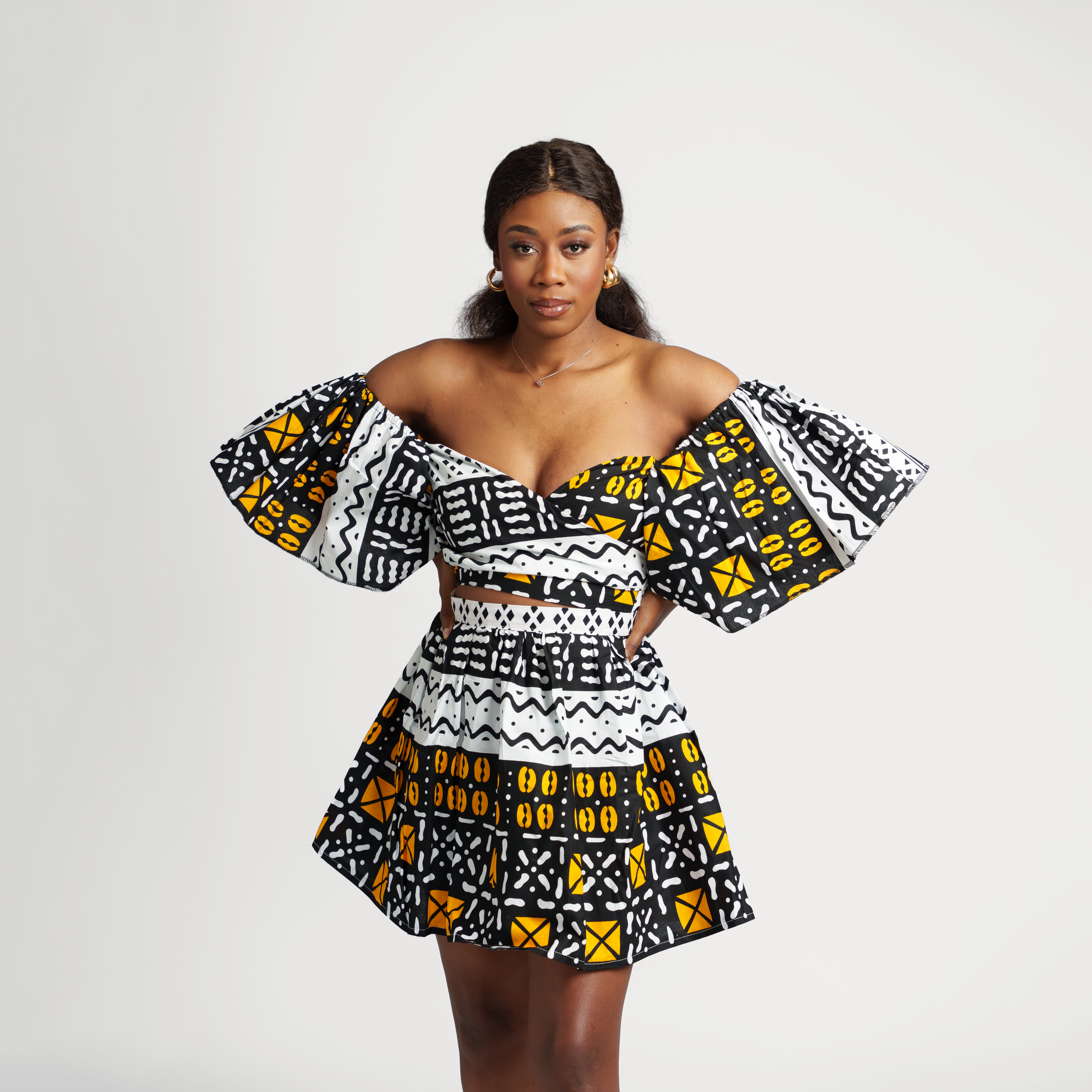 Off-shoulder dress featuring bold black and yellow African print patterns with flared sleeves.