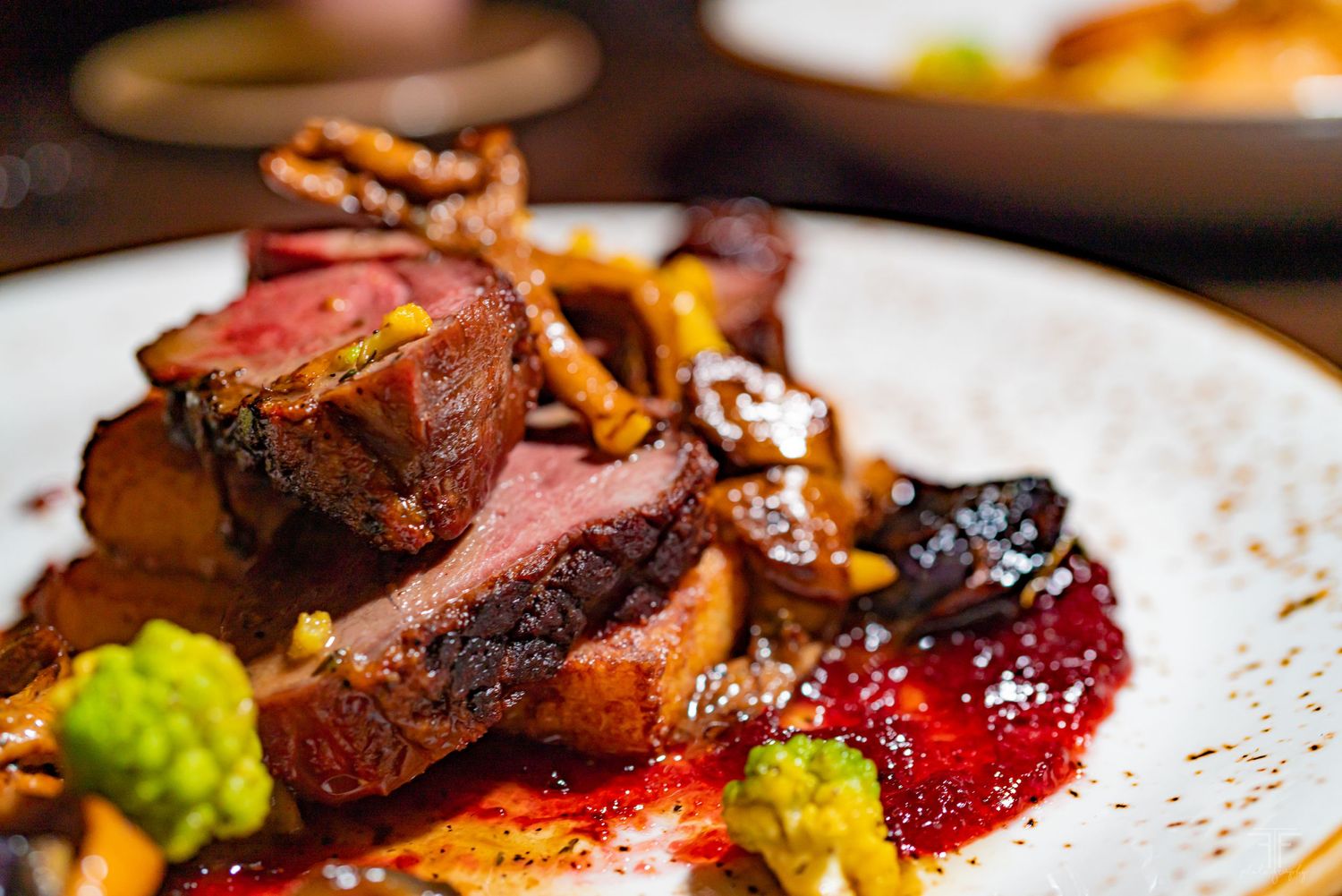 Seared duck breast with berry sauce and seasonal vegetables on white plate.