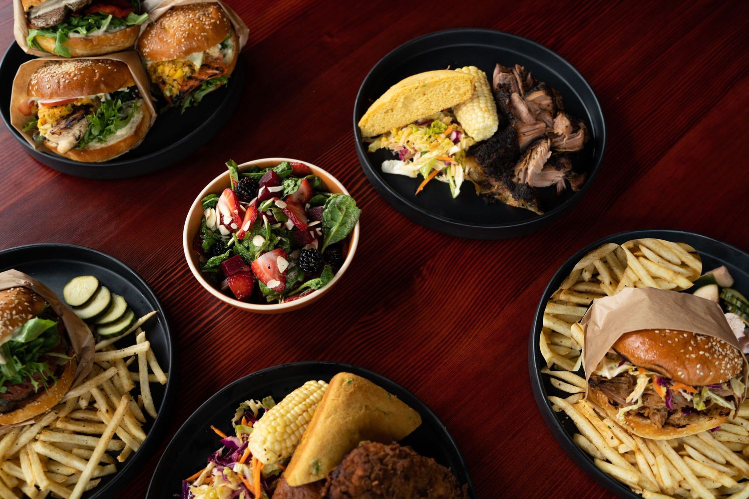 Gourmet burgers and fries served on dark wooden table in restaurant setting.