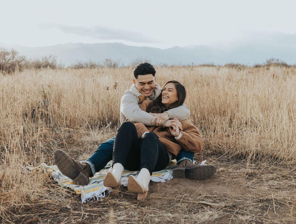 Happy couple sitting on blanket in field of dry grass enjoying a tender moment together.