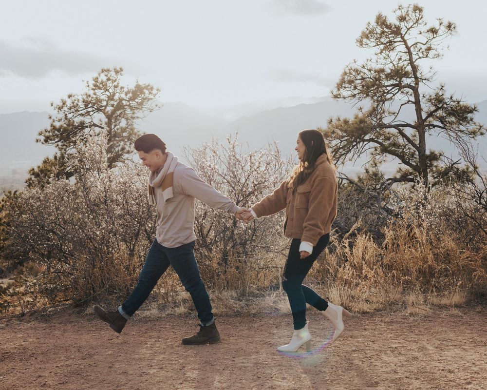Couple holding hands while dancing on a mountain trail surrounded by autumn foliage.