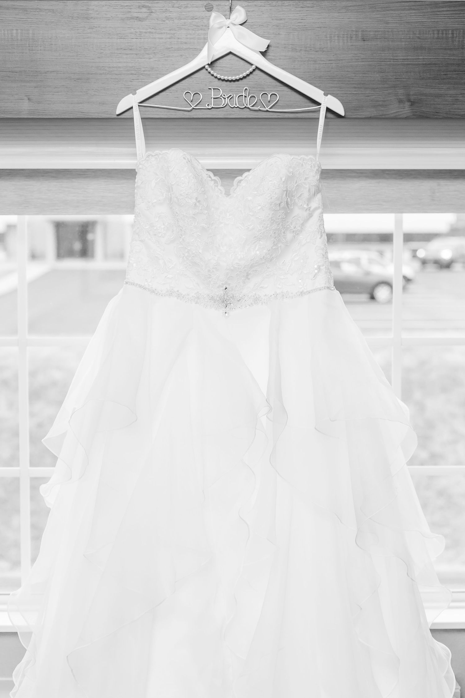 White wedding dress hangs elegantly on personalized bridal hanger against light background.