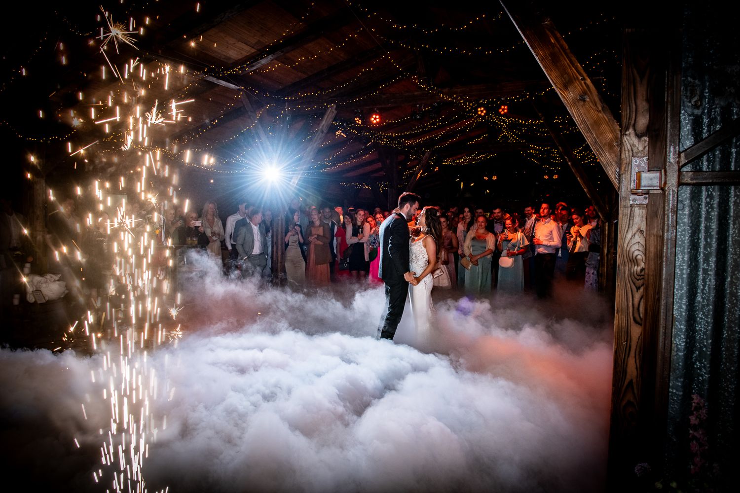 openingsdans van bruidspaar met lage rook en ijsfontein op hun barn wedding in een schuur
