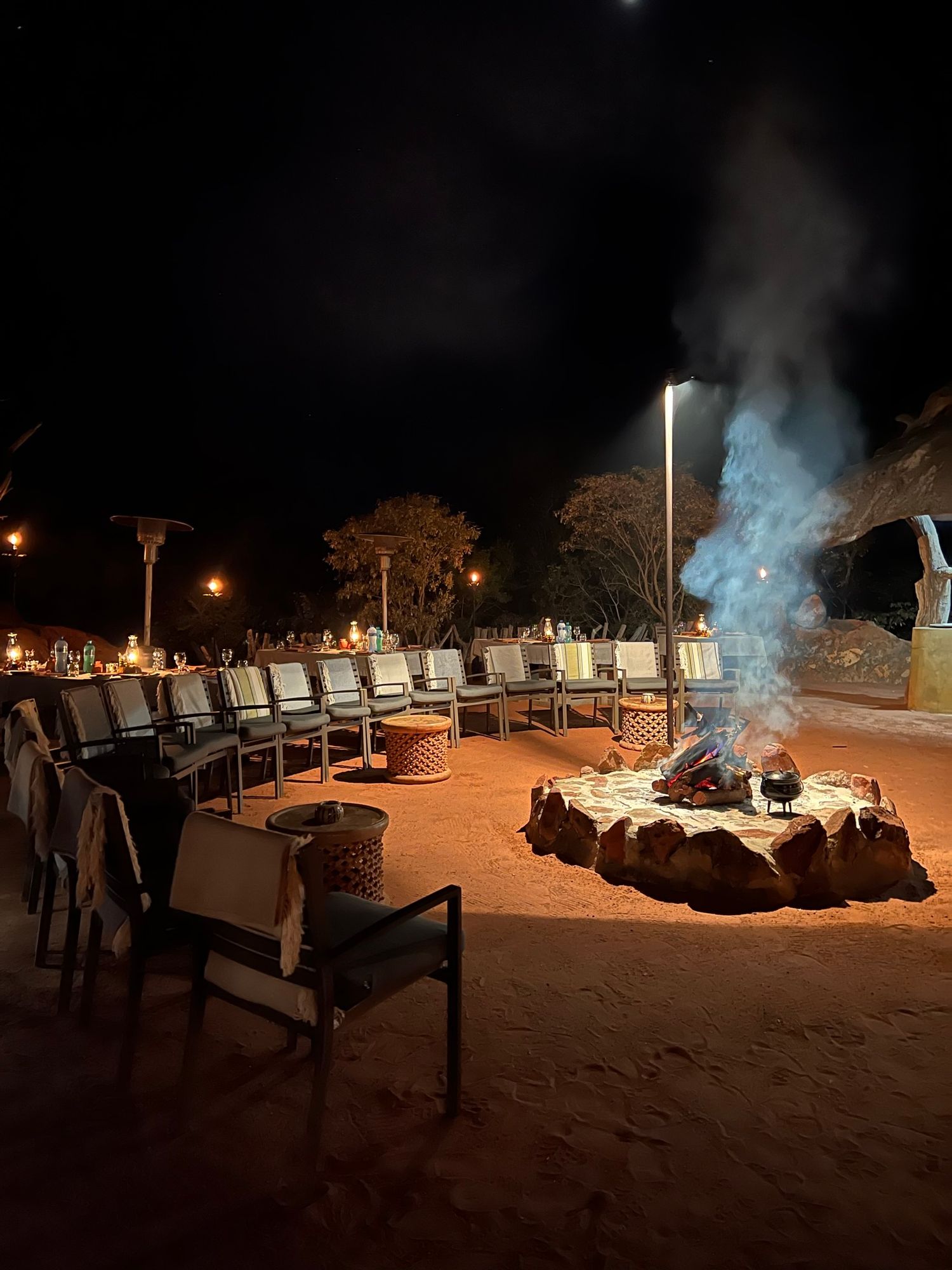 Outdoor nighttime scene with illuminated lounge chairs and fire pits creating a cozy ambiance.