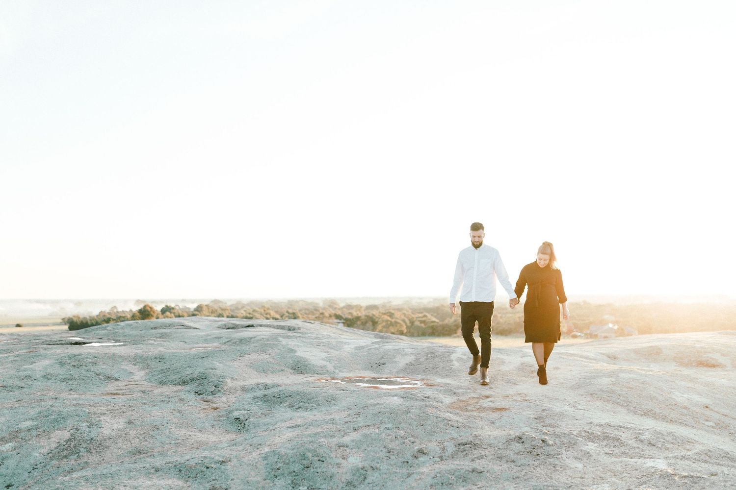 Couple walks together on rocky landscape during golden hour.