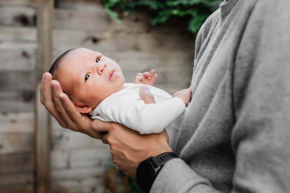 Newborn baby rests peacefully in caregiver's hands against wooden backdrop.