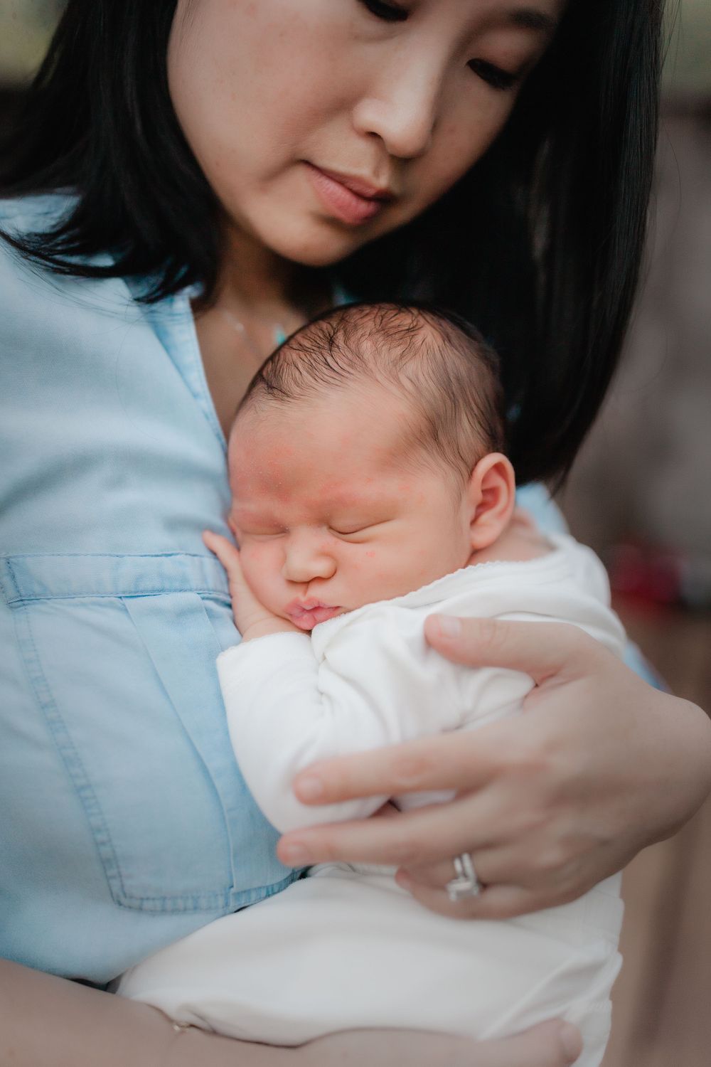 Sleeping newborn baby snuggles against caregiver wearing light blue denim shirt.