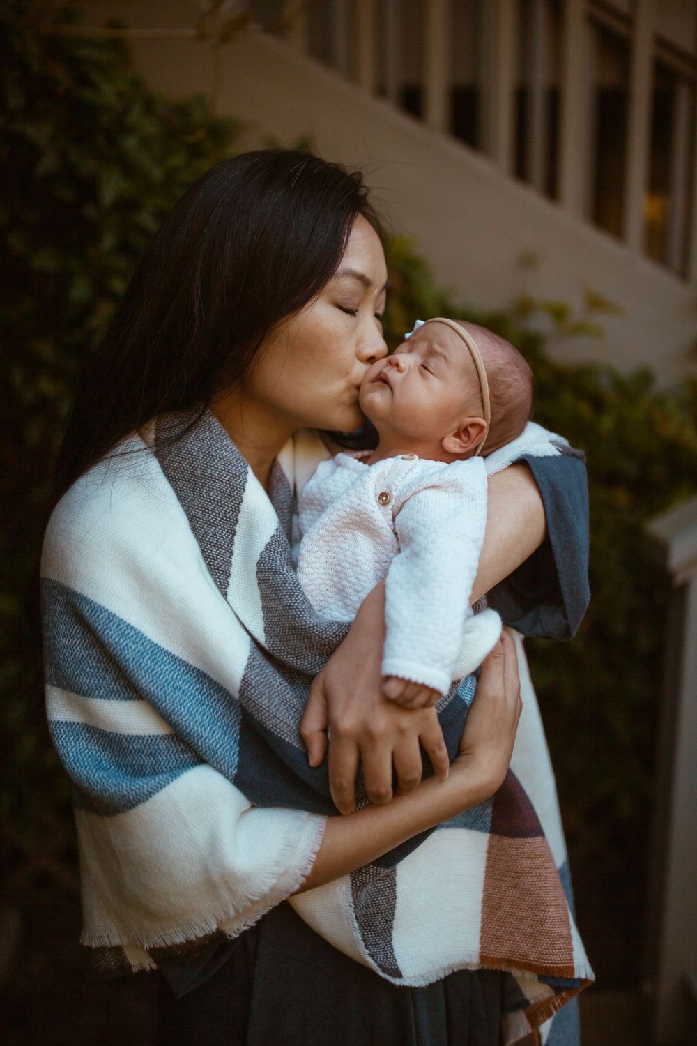 Gentle moments between parent and baby wrapped in white blanket outdoors.