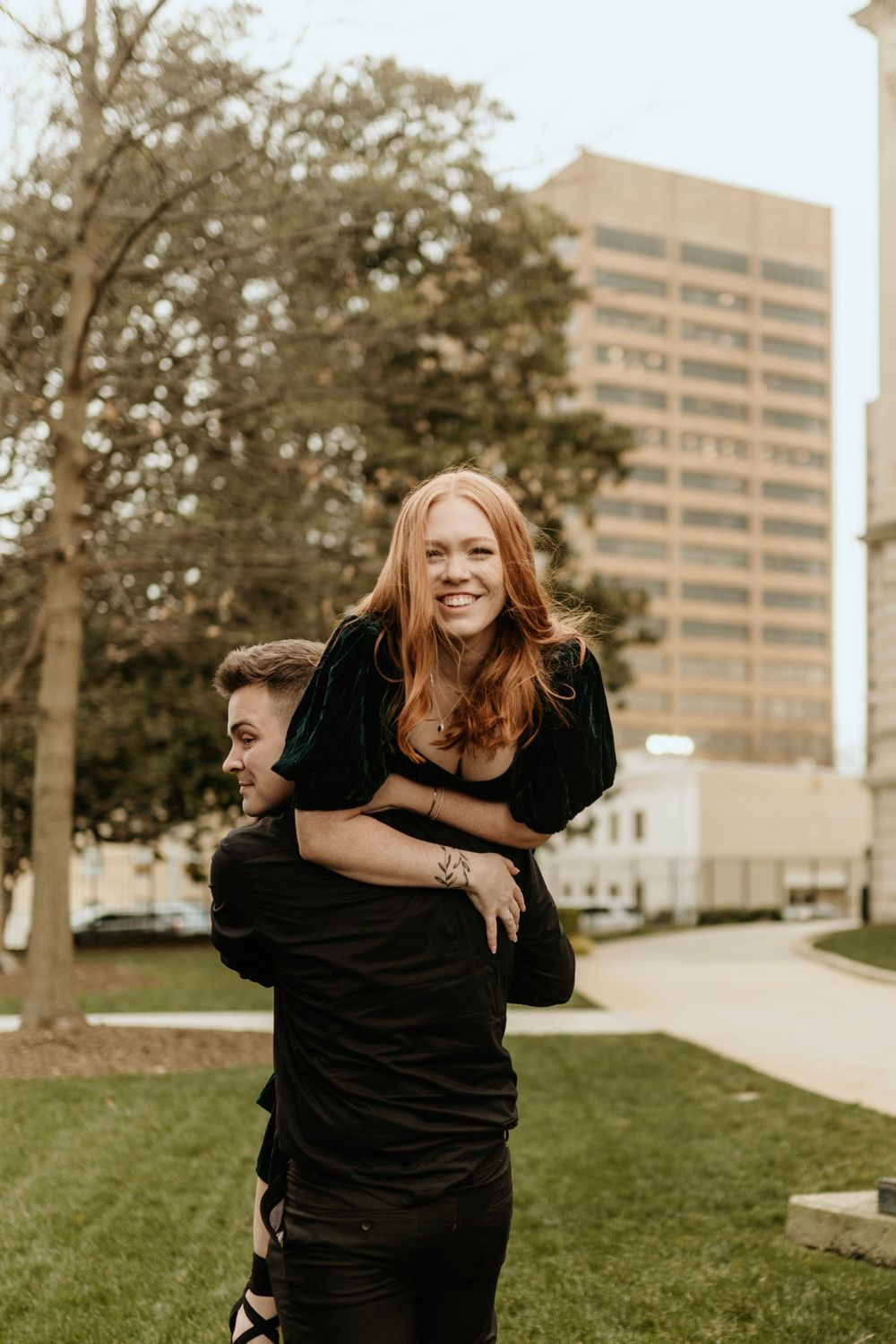 A joyful piggyback ride moment captured in front of a tall urban building on a grassy lawn.