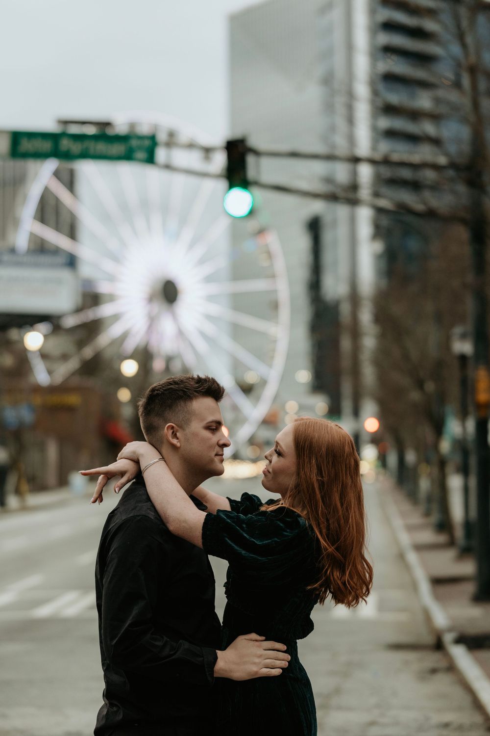 A romantic embrace on a city street with an illuminated Ferris wheel in the background.
