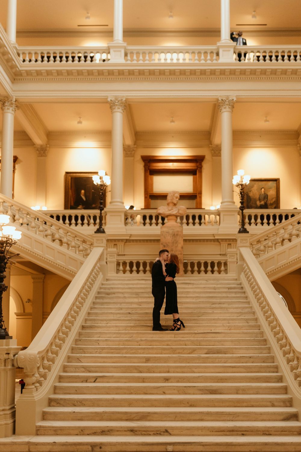 Elegant engagement portrait on grand white marble stairs in a historic building.