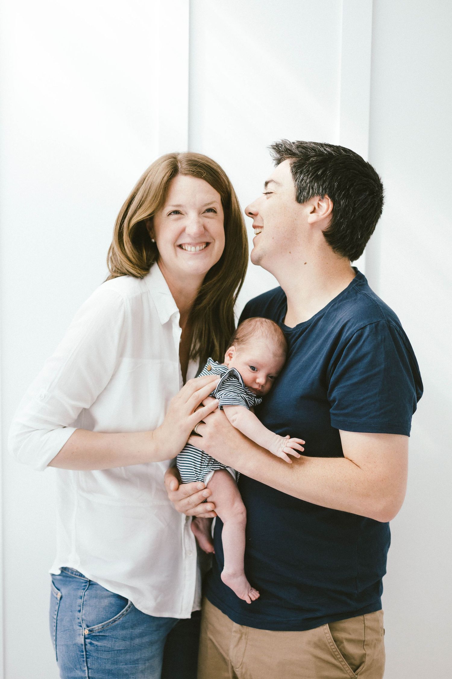 Parents share joyful moments with their newborn baby against a white backdrop.