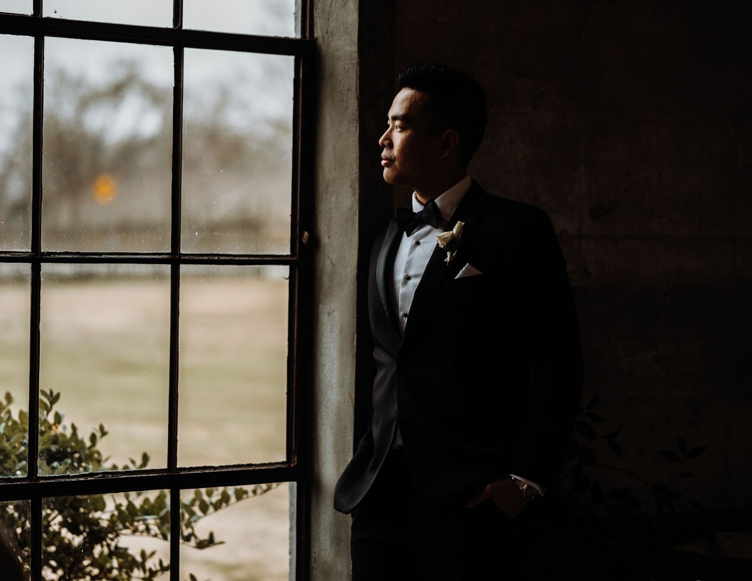 Formal attire silhouette against large window in moody lighting.