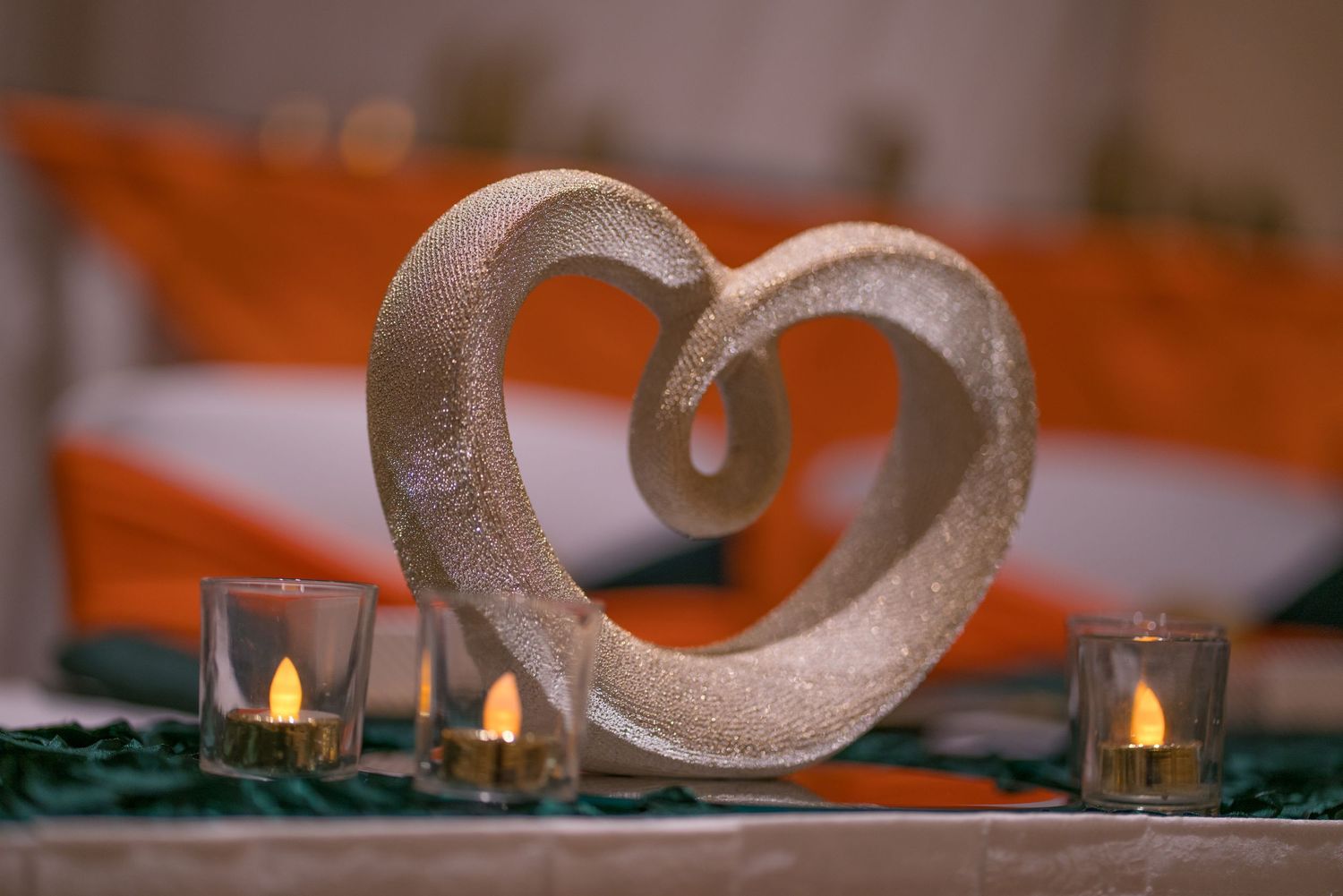 A silver decorative heart sculpture sits among small glowing candles on a dark table.