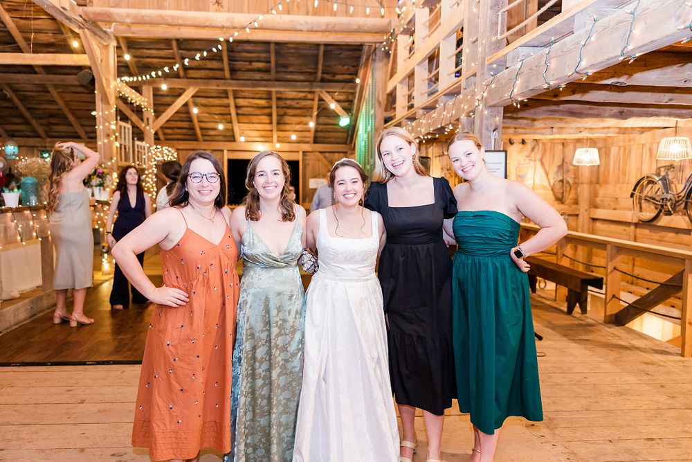 Wedding party members posing together in rustic barn venue with string lights.