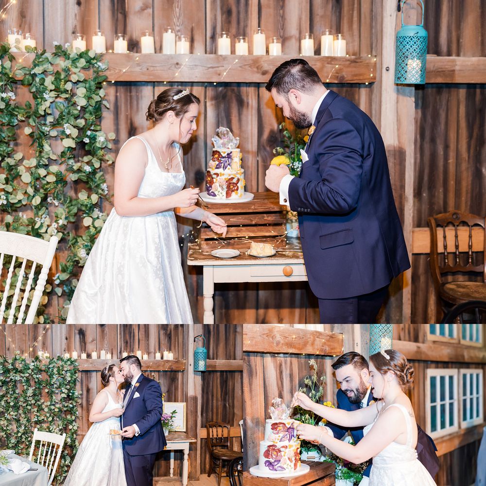 A couple cuts their rustic wedding cake together in a barn-style venue decorated with greenery and candles.