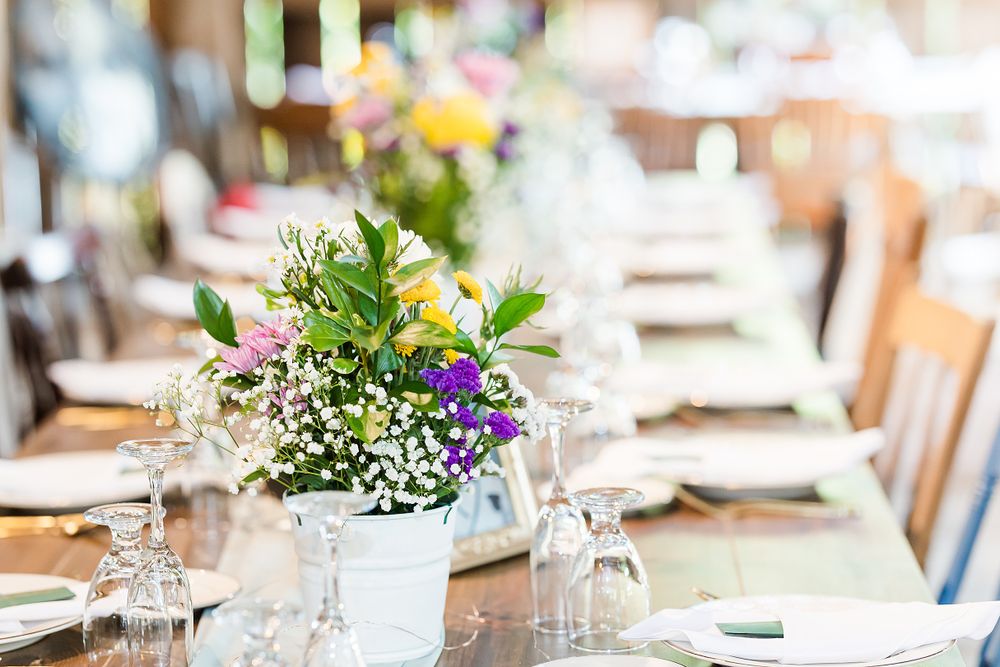 Elegant wedding table setting with white wildflower centerpiece in rustic vase and wine glasses.