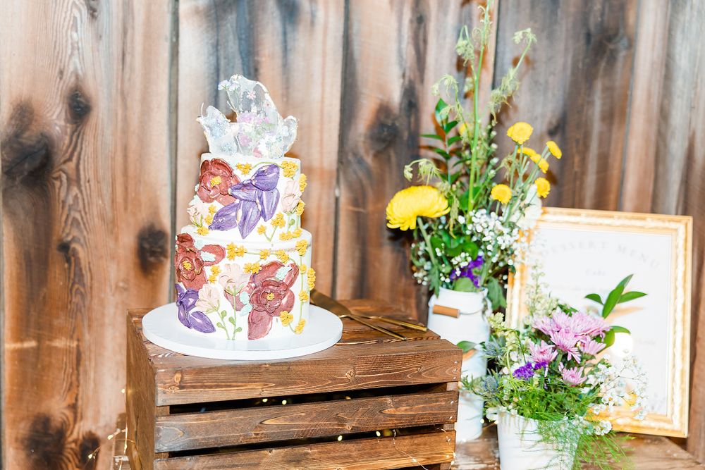 Whimsical wedding cake display with colorful decorations and fresh floral arrangements.