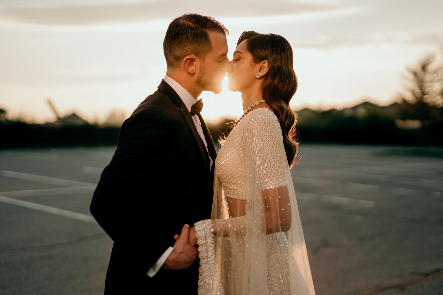 A romantic sunset silhouette of a couple sharing a tender moment in a white wedding dress and suit.