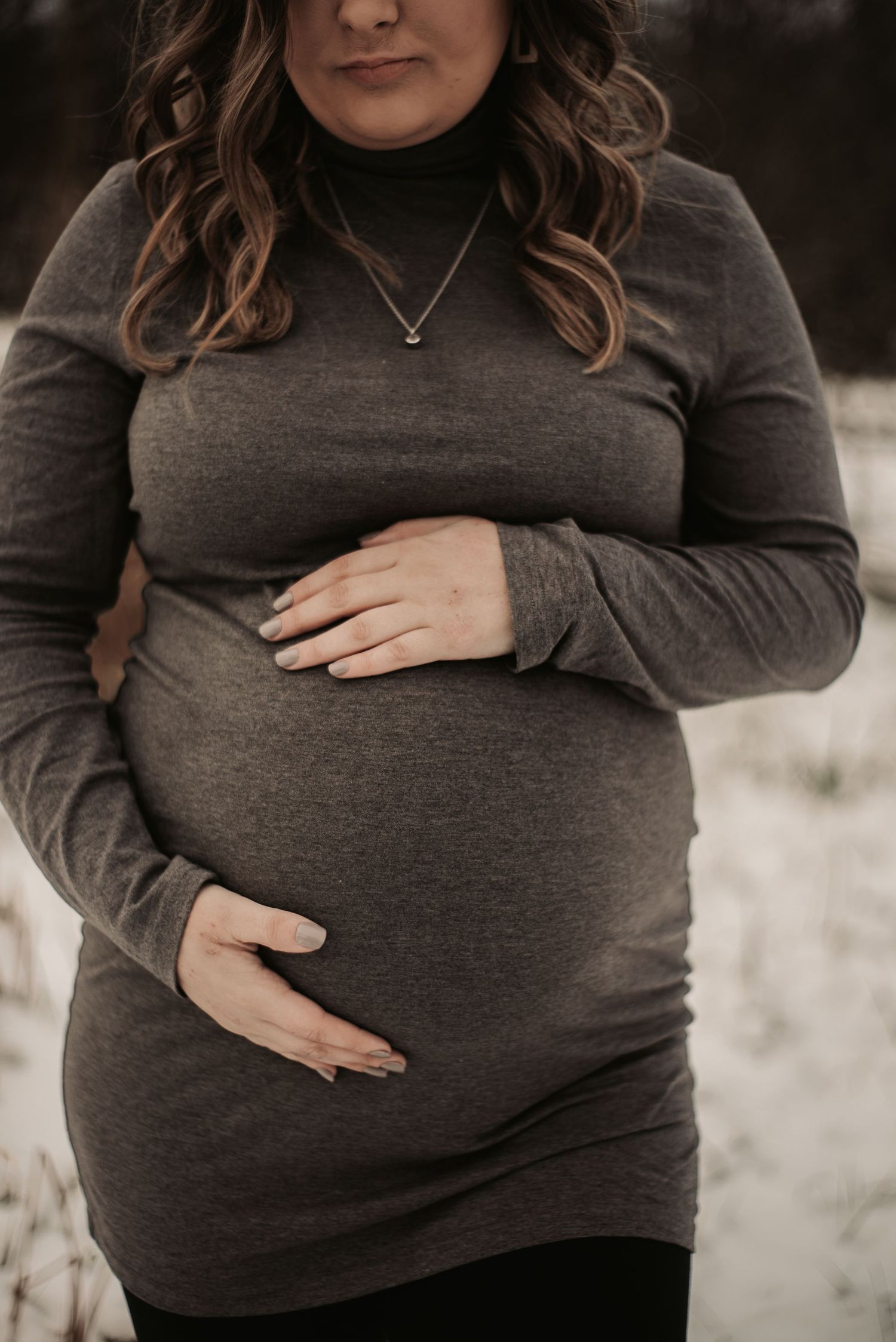 A maternity photo showing hands cradling a baby bump in a grey sweater.