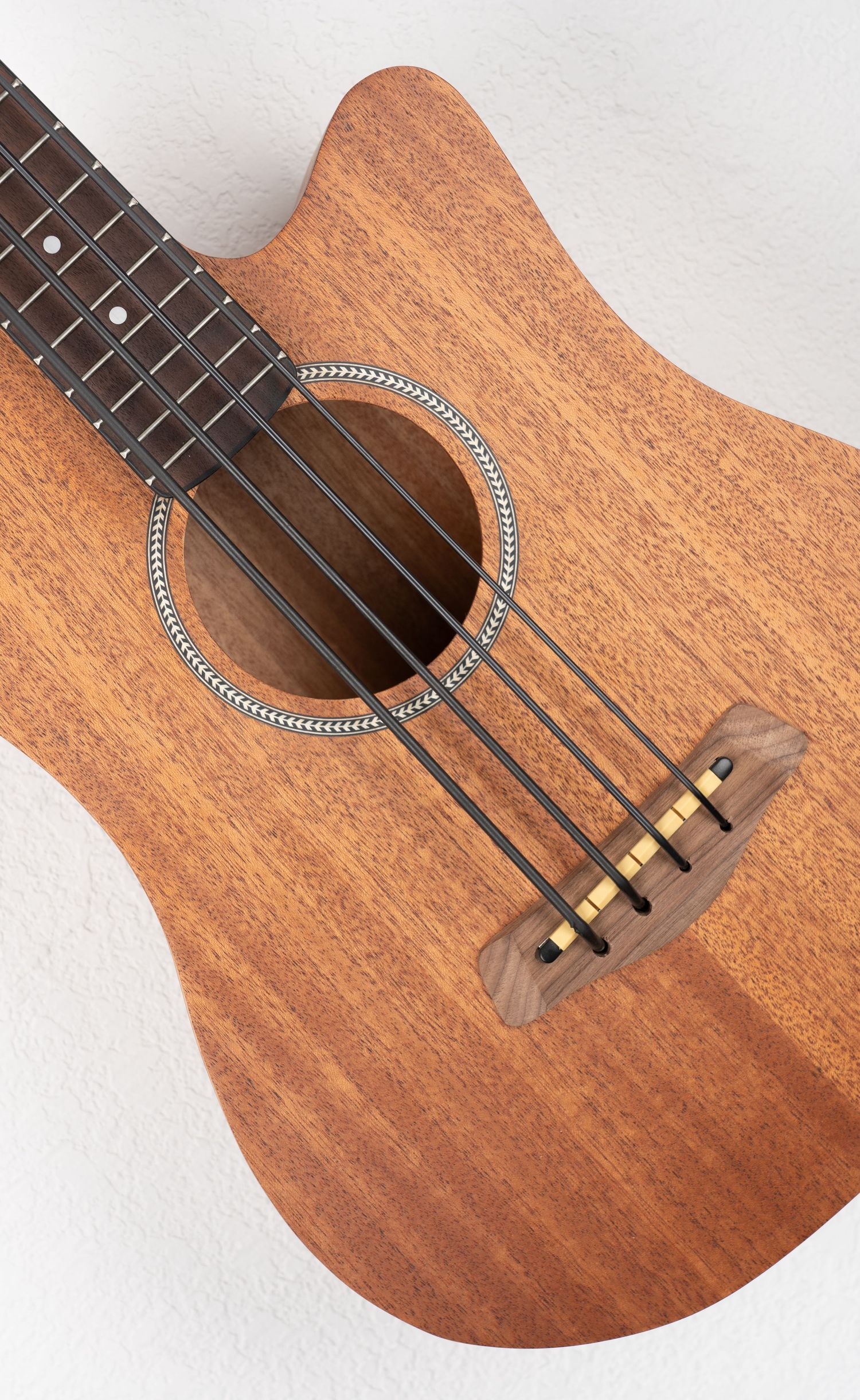 Close-up of acoustic bass guitar sound hole showing four strings and decorative rosette pattern.