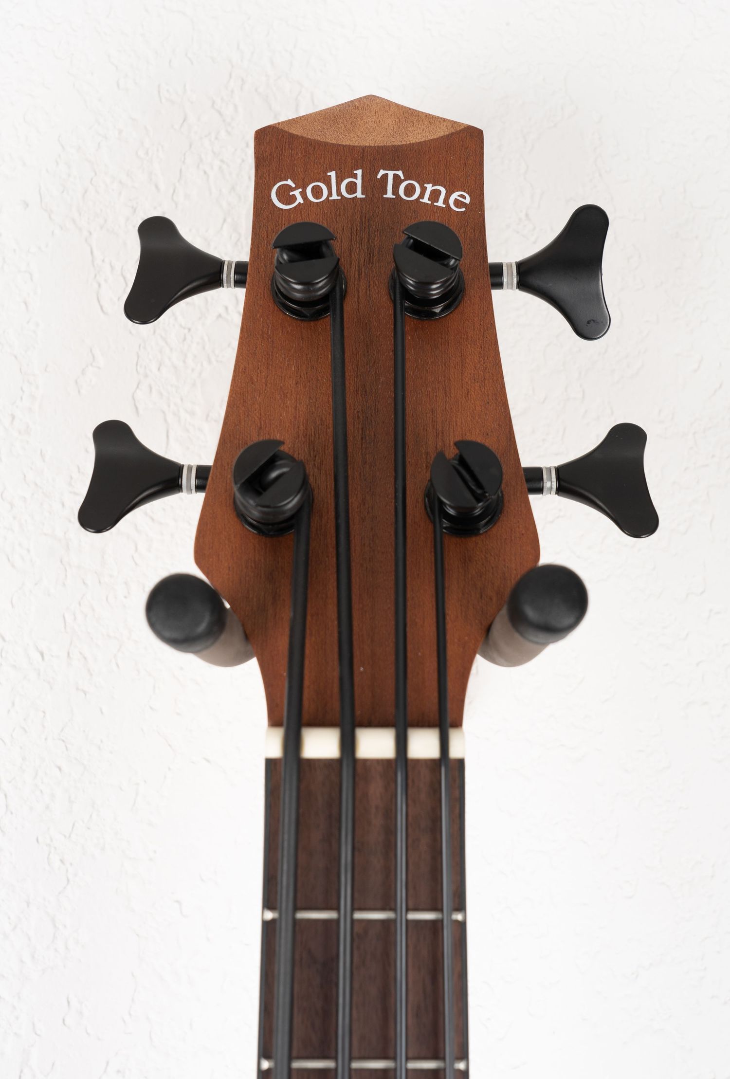 Gold Tone branded headstock of acoustic bass guitar with black tuning machines.