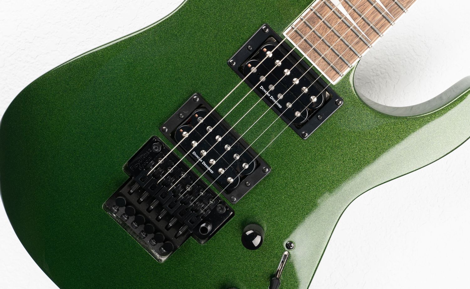 Close up of green electric guitar body showing dual black humbucker pickups.
