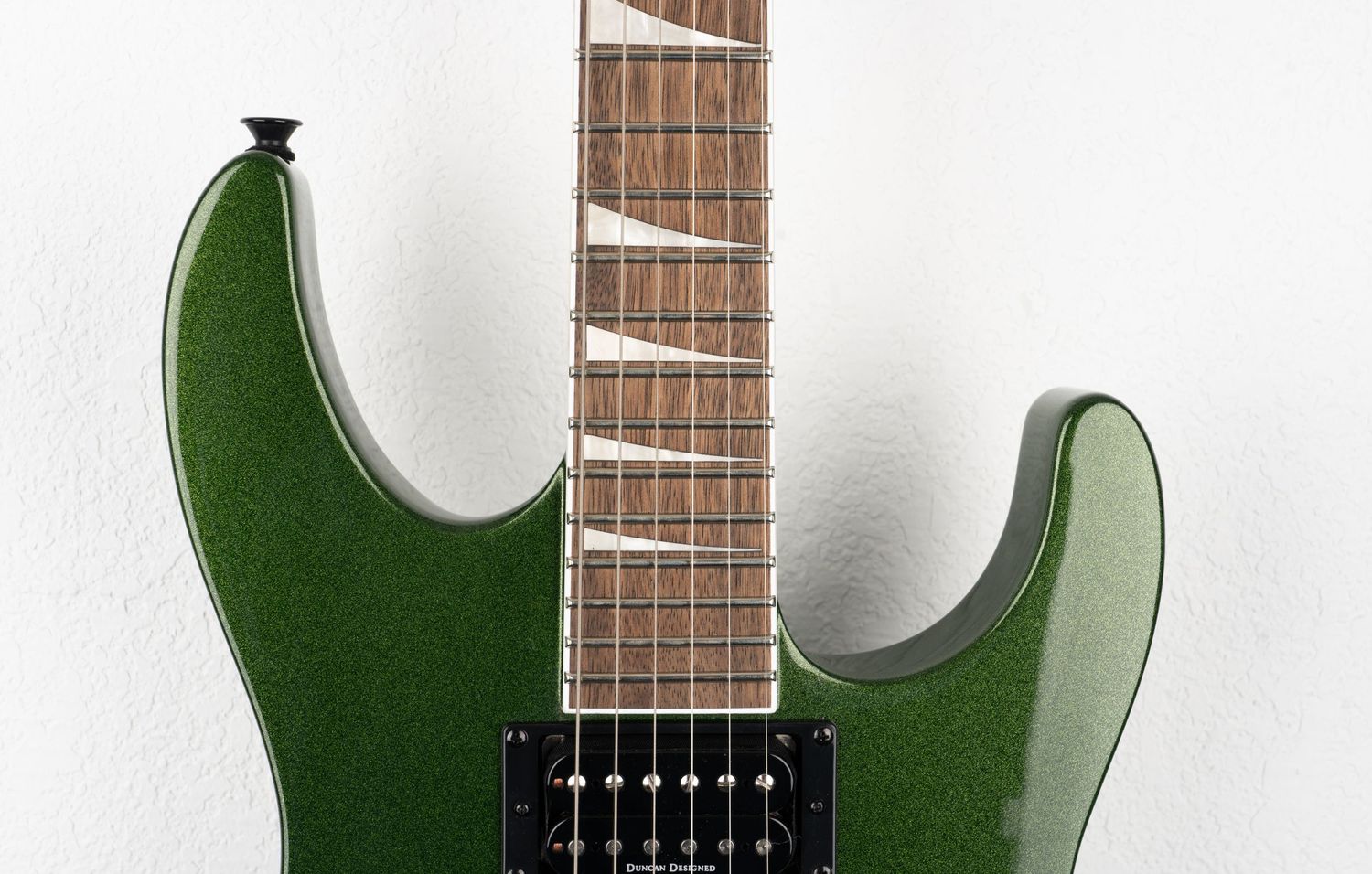 Detail shot of green electric guitar showing neck joint and pickups.