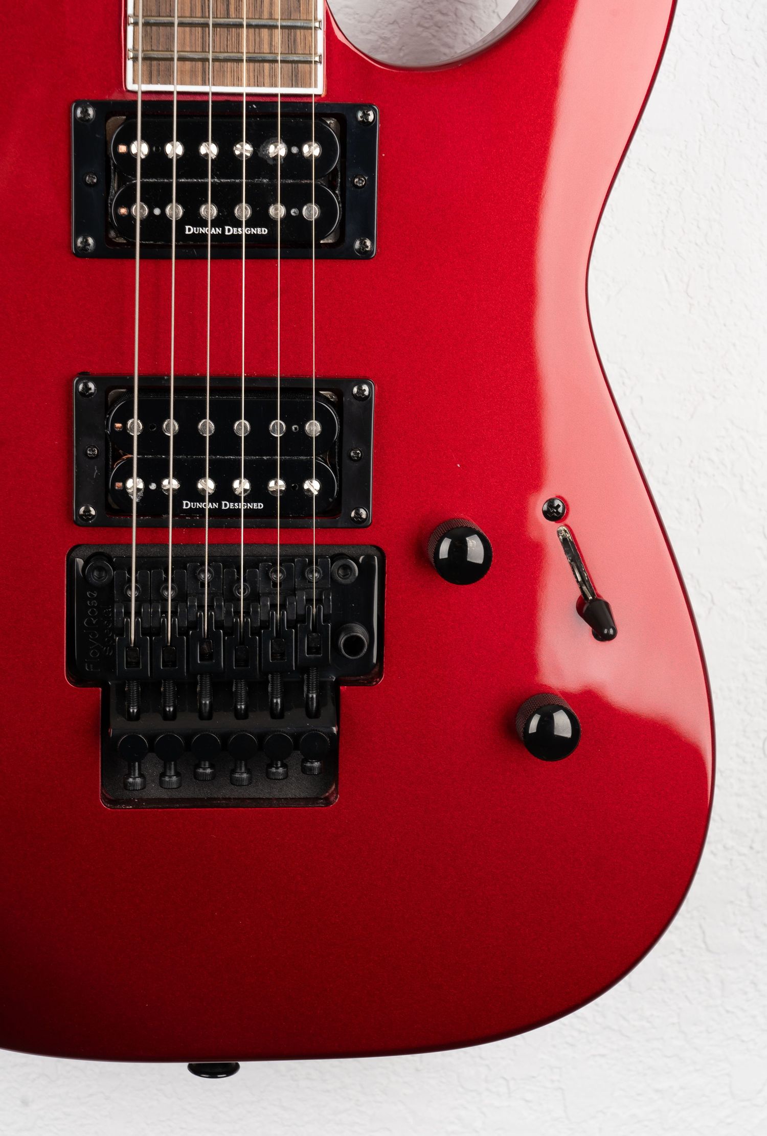 Close up detail of red guitar's dual humbuckers and Floyd Rose bridge system.