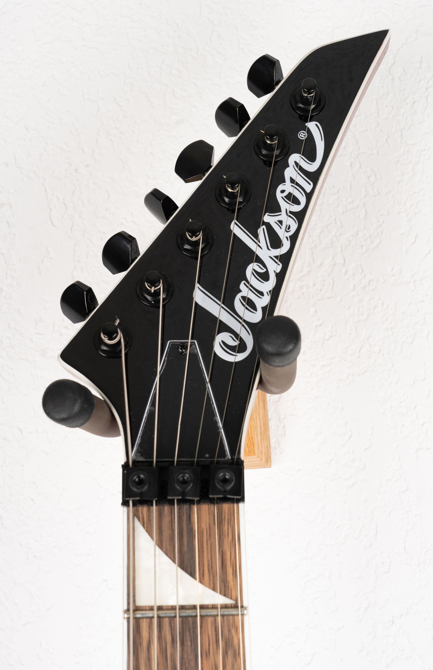 Jackson guitar headstock with black tuning pegs and logo against white background.