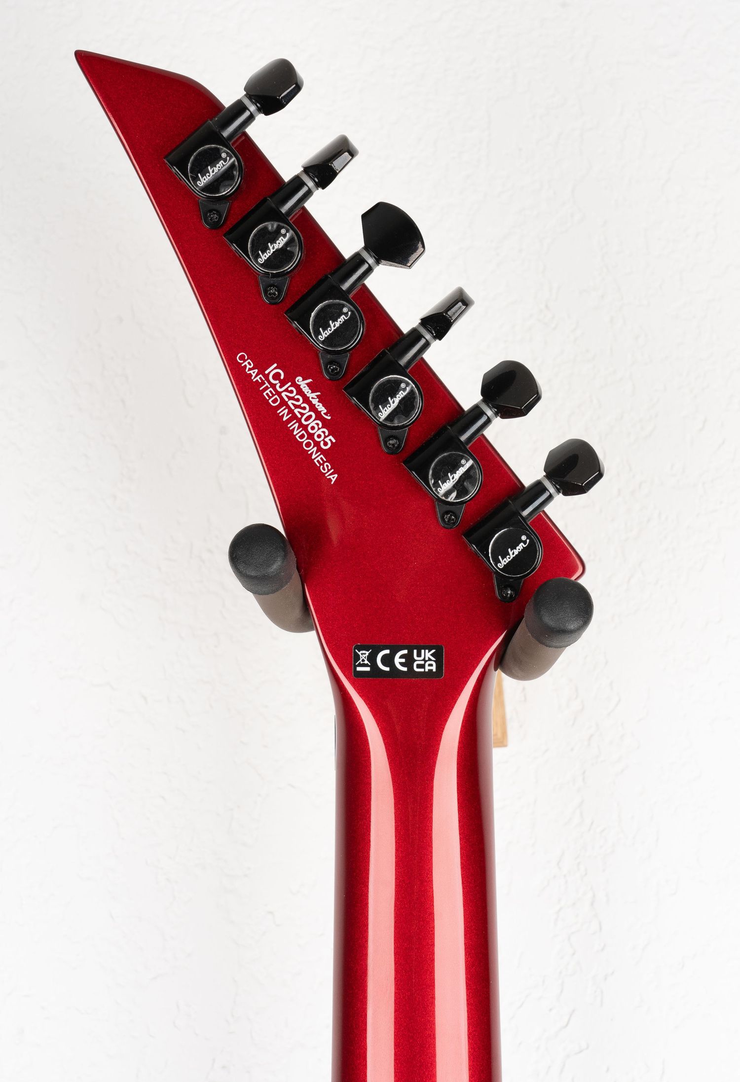 Red Jackson guitar headstock with black tuning machines against white background.
