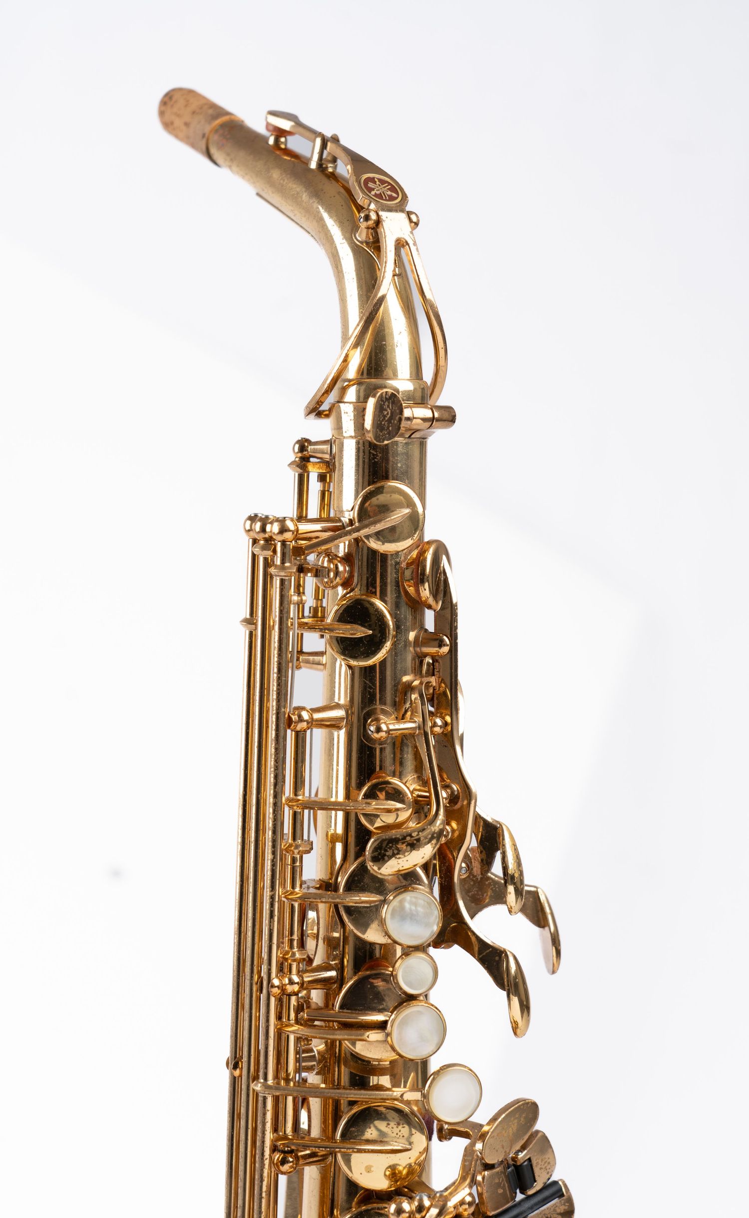Close-up view of a golden alto saxophone's neck and key mechanism against white background.