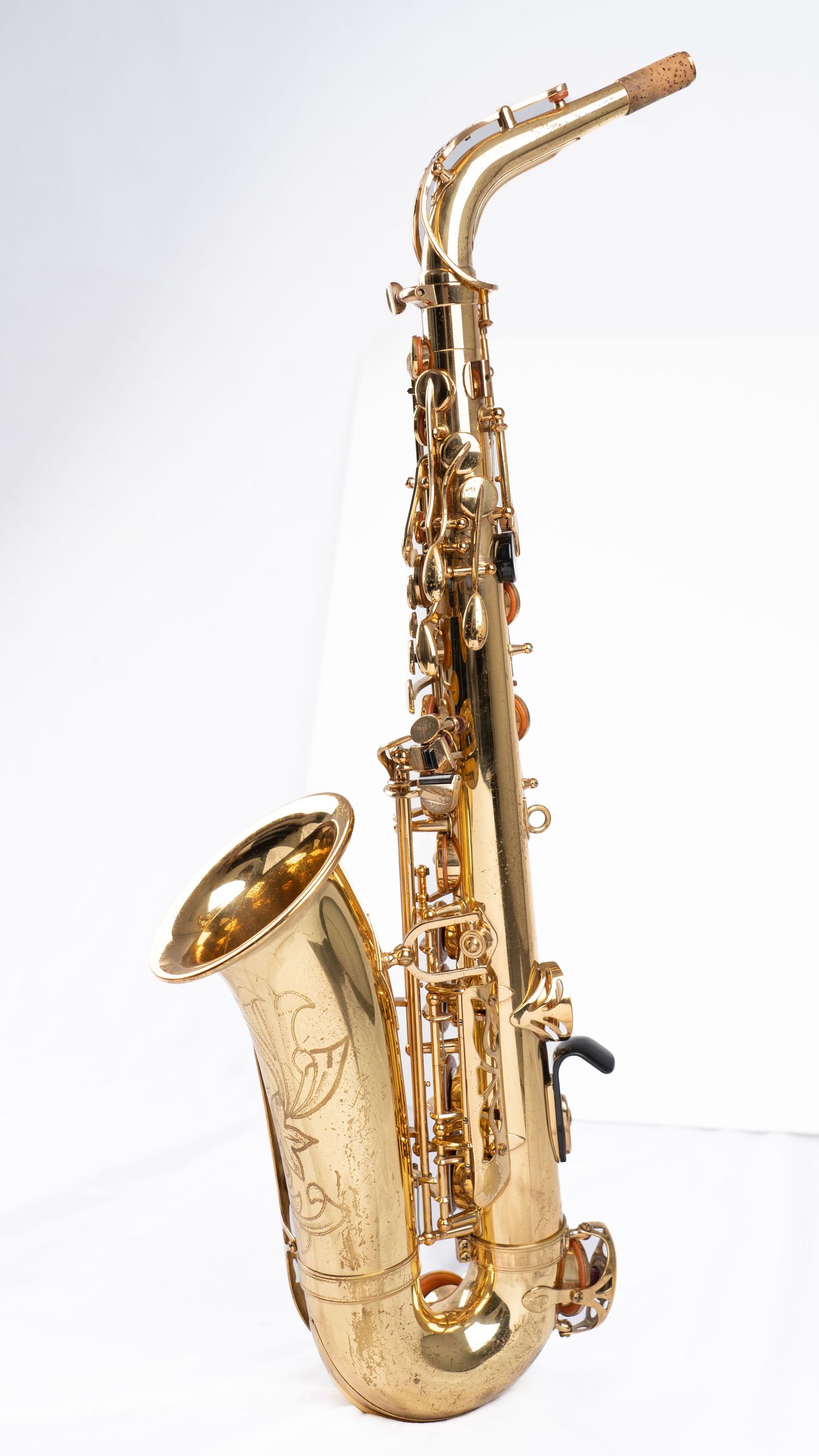 Complete view of a polished brass alto saxophone with engraved bell against white background.