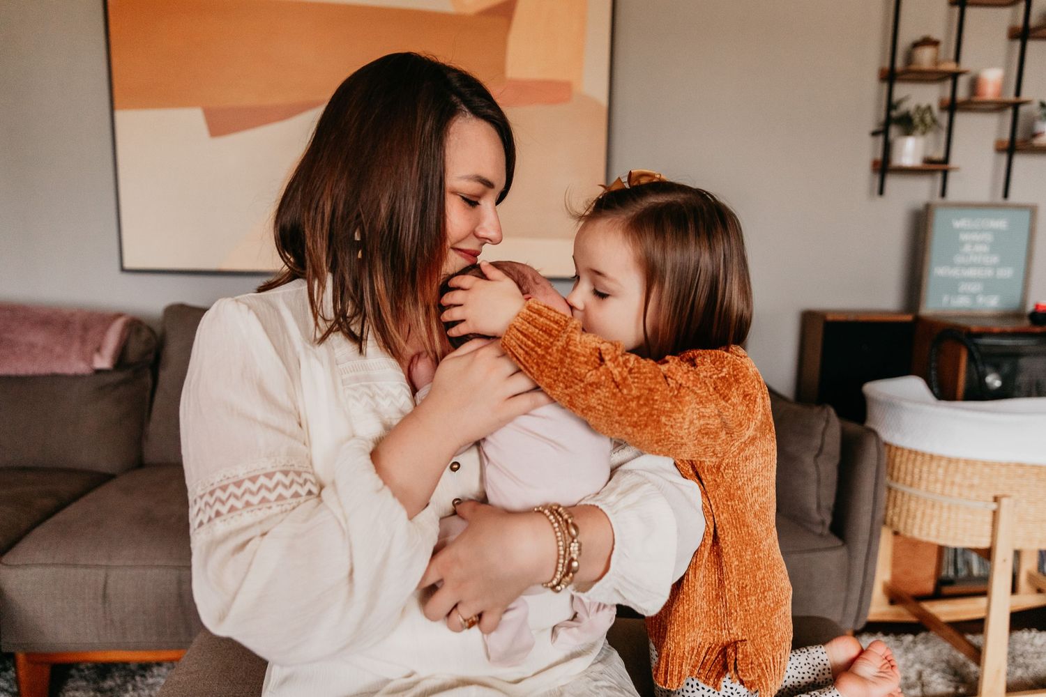 Candid portrait of a mother holding her newborn daughter while her preschooler kisses the baby from the other side.