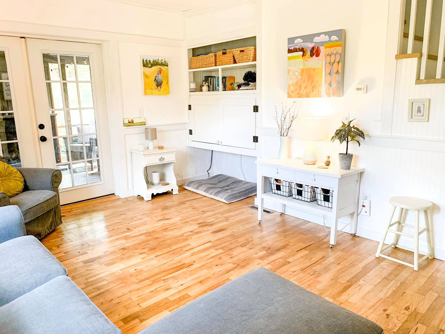 Modern living room interior with light hardwood floors, white walls, and natural sunlight streaming through windows.