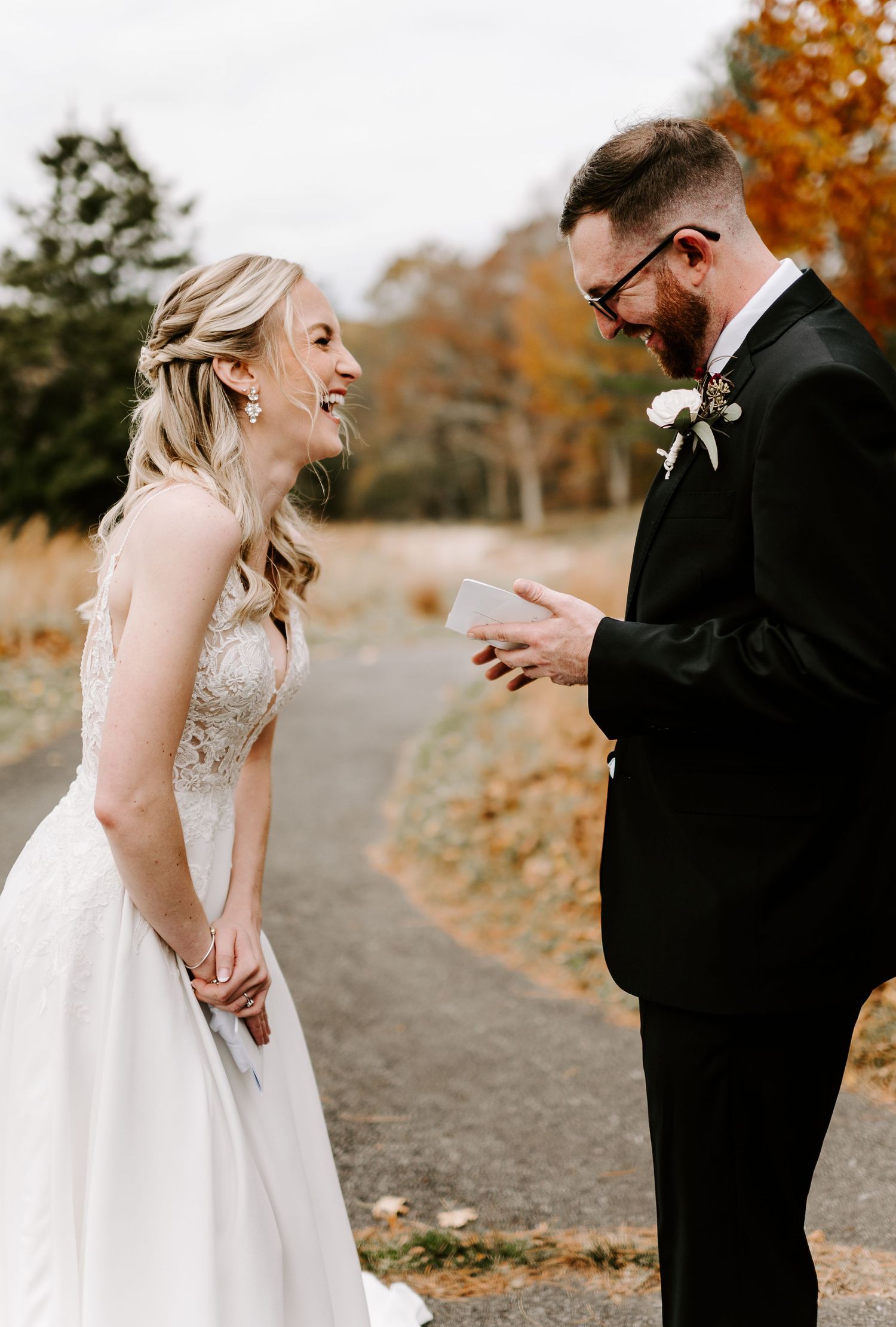 Emotional first look between newlyweds on a path with golden autumn trees in background.