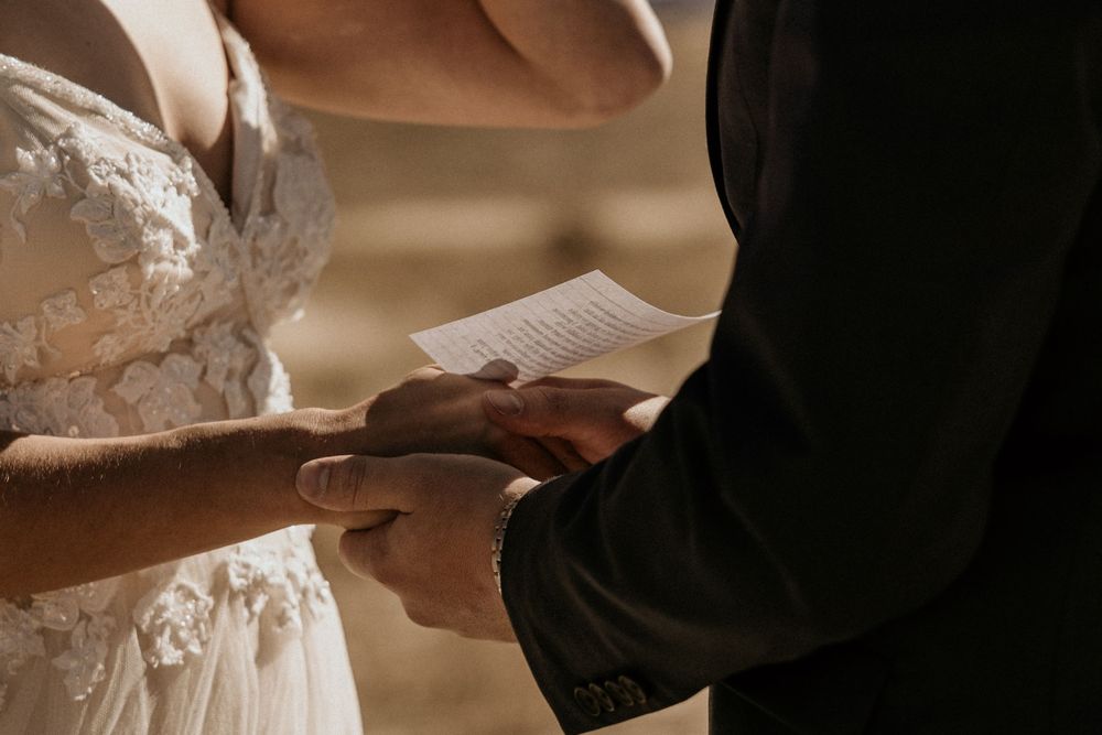 Close-up of bride and groom holding hands while exchanging written vows during an outdoor ceremony.