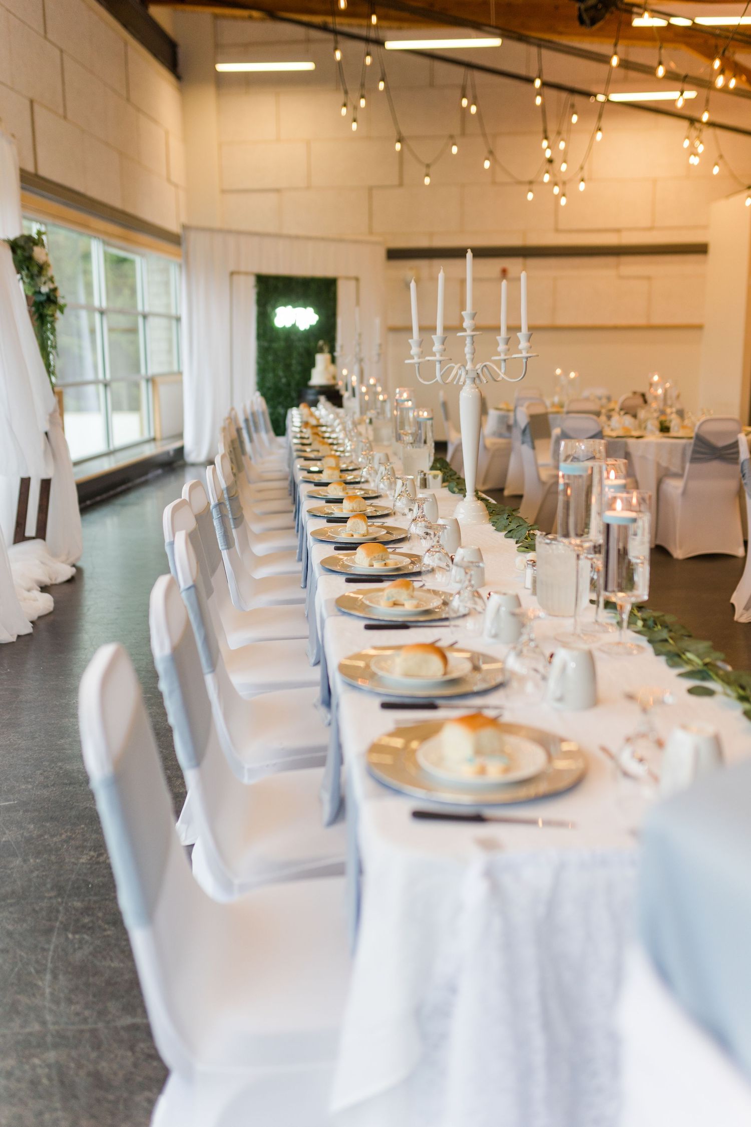 Elegant wedding reception tables set with white linens and place settings under string lights.