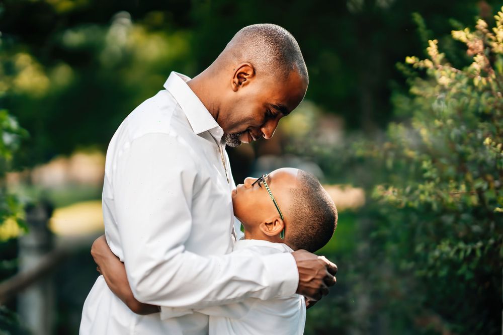 A tender embrace captured between two people wearing white against a garden background.