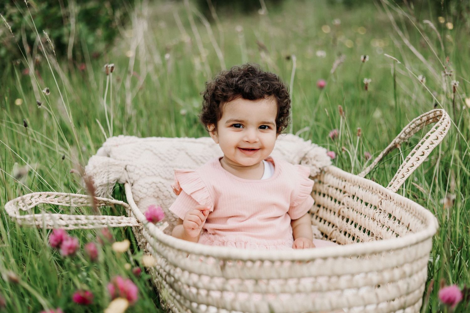baby girl sitting in a basket in a meadow