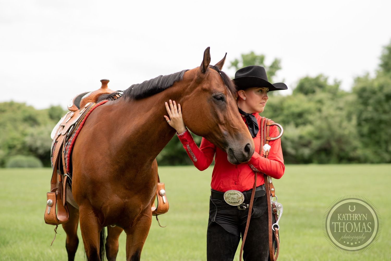 Handler in red western shirt shares affectionate moment with brown horse in grassy field.
