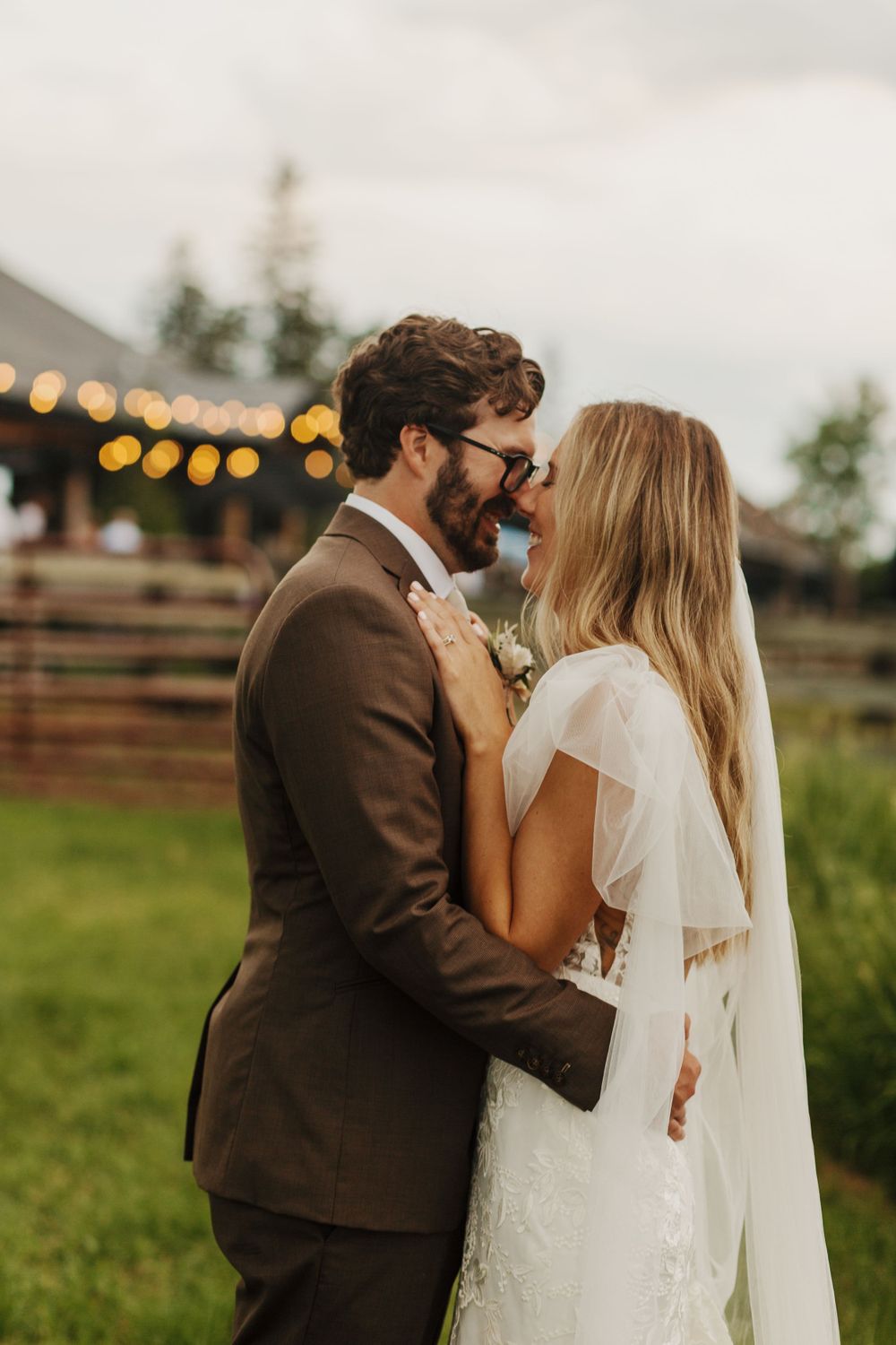 Romantic moment between newlyweds at outdoor reception with string lights in background.