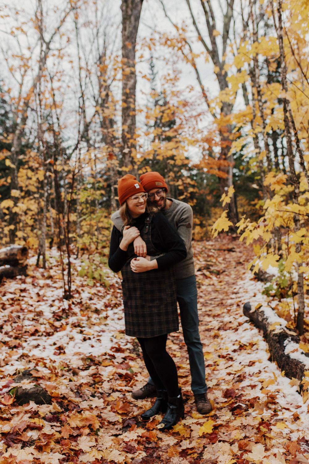 Couple embraces among fallen autumn leaves in a forest setting.