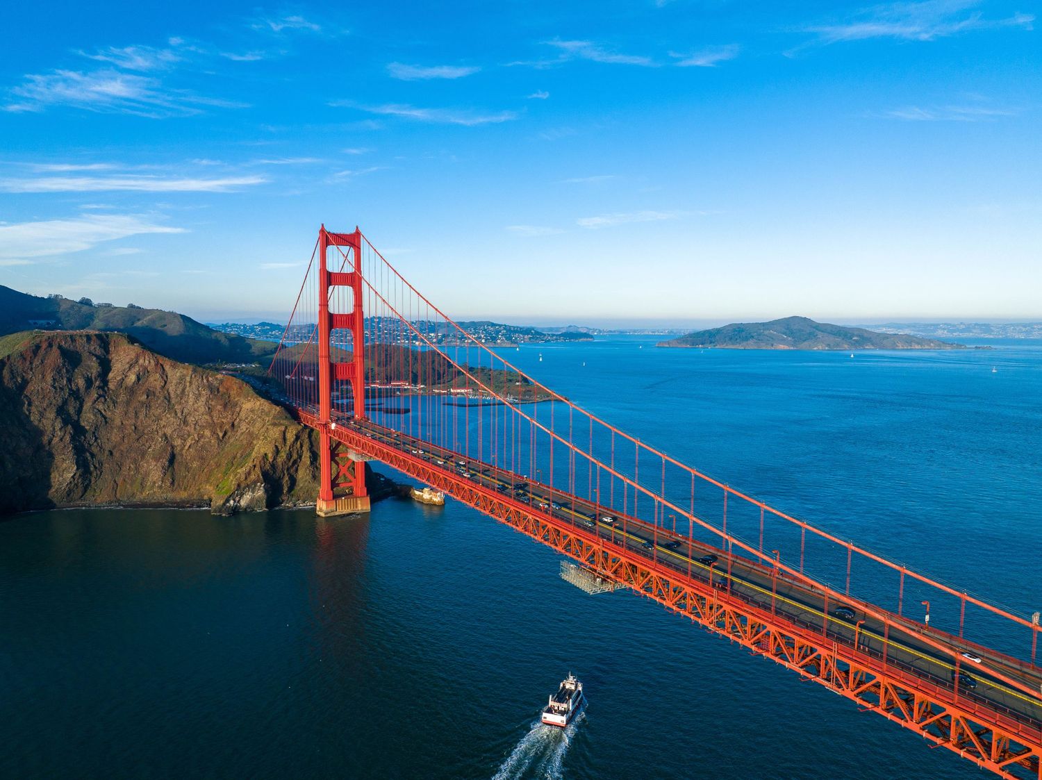 Aerial view of the Golden Gate Bridge spanning San Francisco Bay with a boat passing underneath.