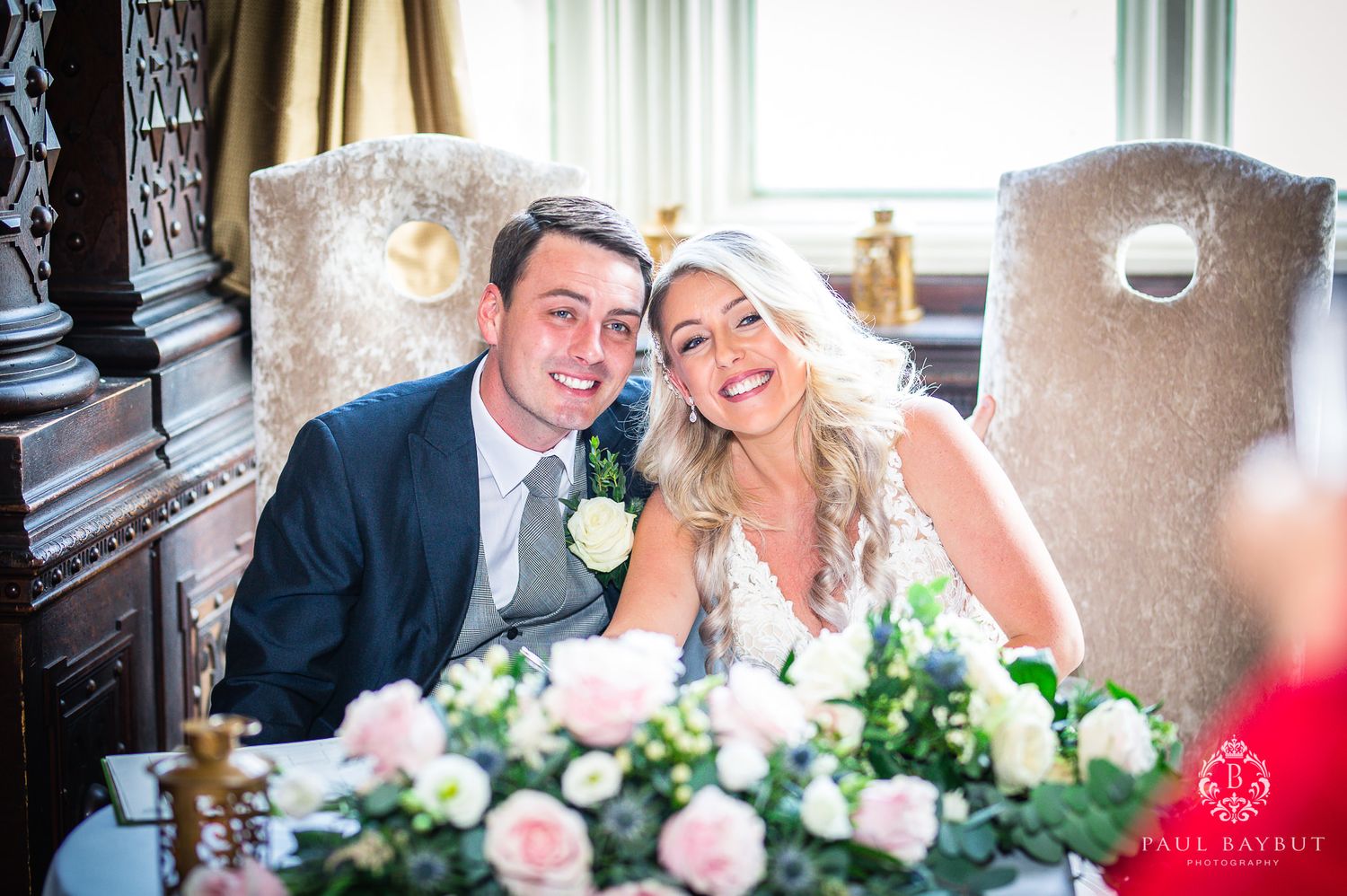 Newlyweds share a joyful moment at their reception table decorated with pink and white flowers.