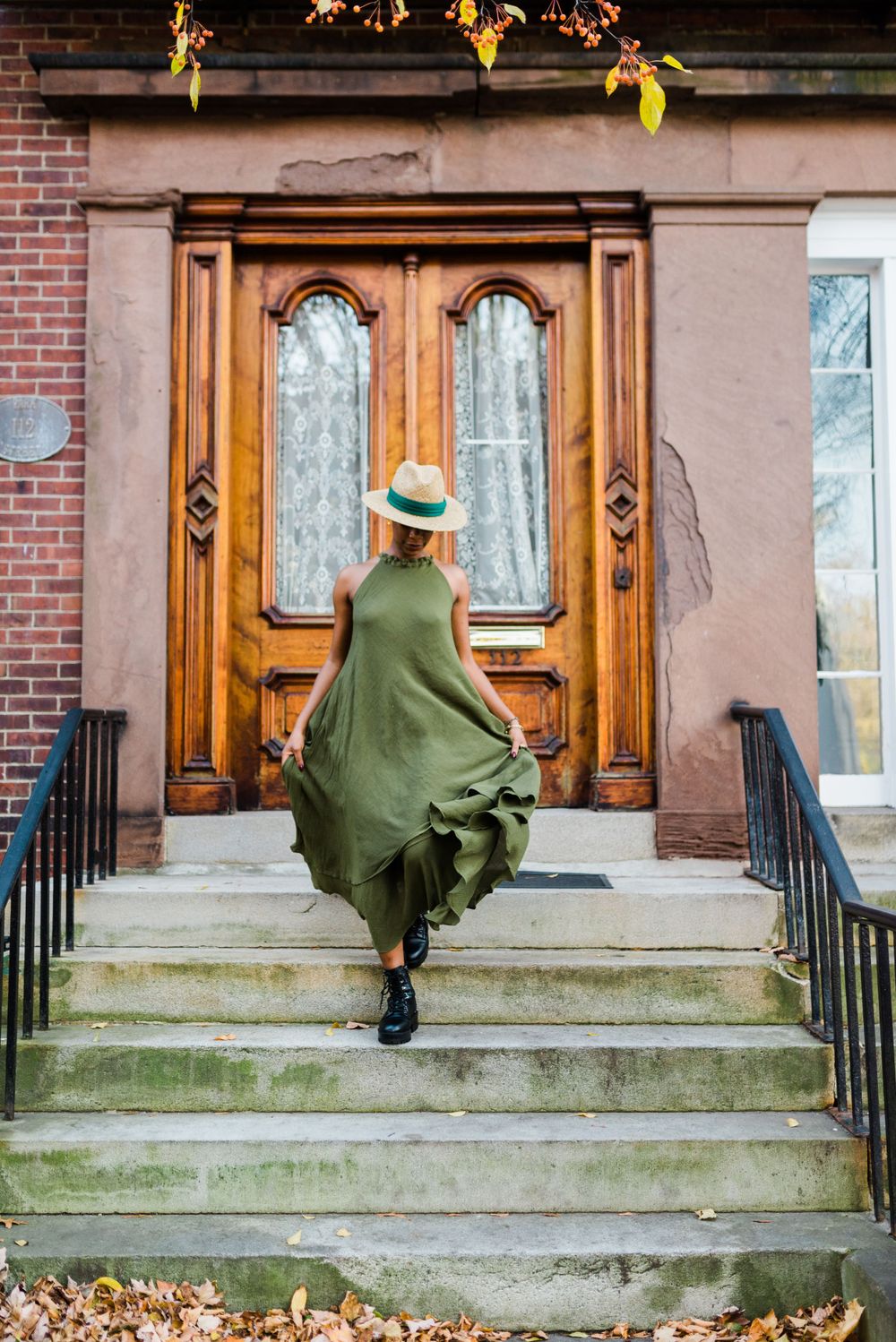 An elegant olive green dress flows in motion ascending brownstone steps with wooden doors.