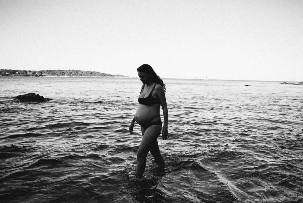 A silhouette standing in shallow ocean water during golden hour.